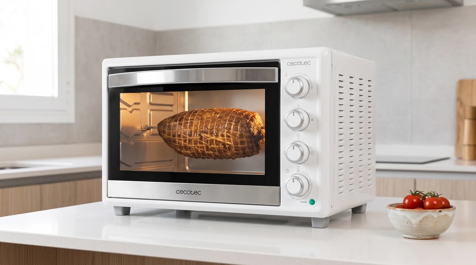 Mini forno elétrico Cecotec Bake&Toast 4600 Gyro branco sobre uma bancada, com um assado no espeto rotativo.