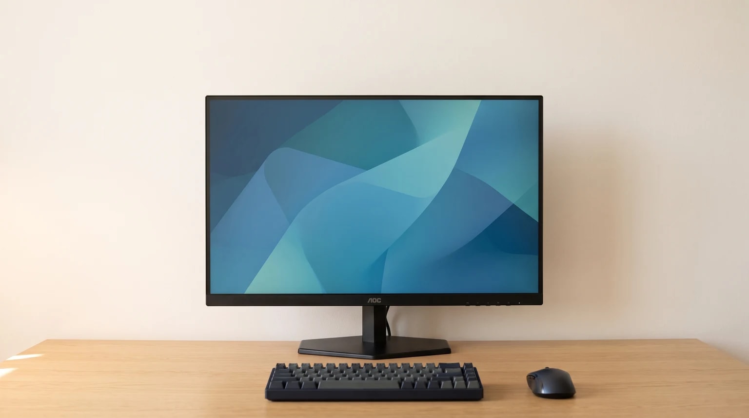 Um monitor AOC preto sobre uma secretária de madeira clara, com um teclado compacto e um rato à sua frente.