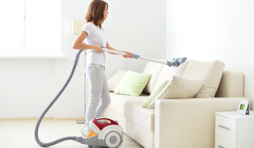 Uma mulher a usar um aspirador horizontal para limpar o sofá.