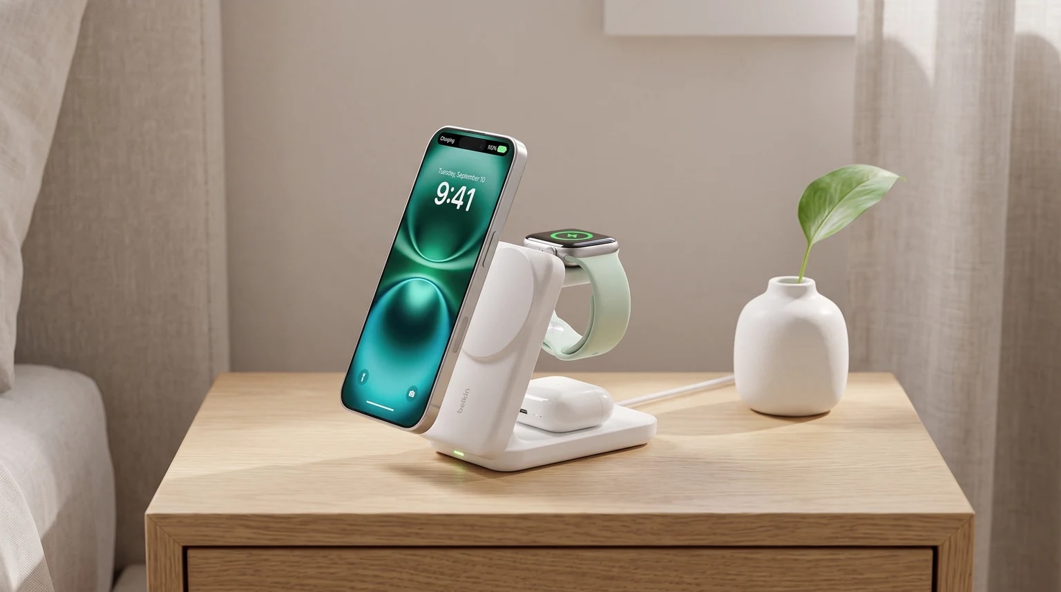 Uma estação de carregamento sem fios 3 em 1 branca numa mesa de cabeceira de madeira, a carregar em simultâneo um iPhone, um Apple Watch e uns AirPods.