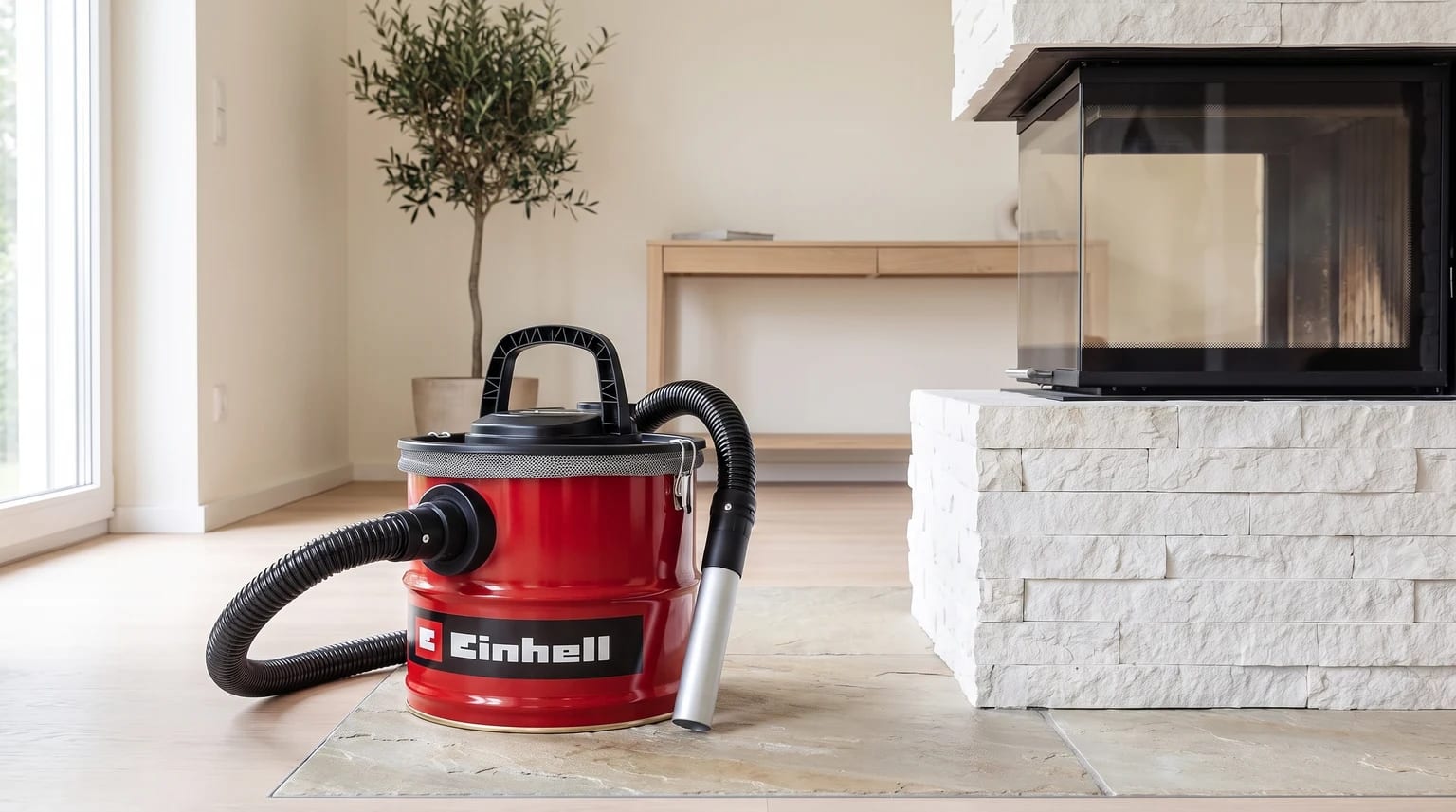 Um aspirador de cinzas vermelho da Einhell no chão de ladrilho, ao lado da base de pedra branca de uma lareira moderna.