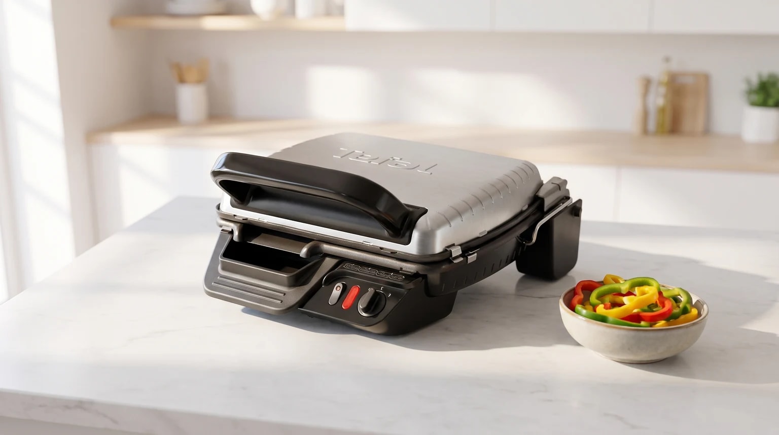 Grelhador elétrico Tefal prateado e preto numa bancada de cozinha, ao lado de uma tigela com pimentos fatiados.