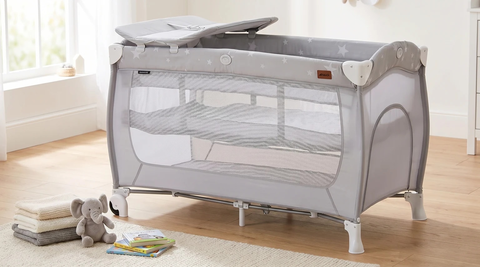 A light grey Hauck Sleep N Play Center travel cot with changing station set up empty in a bright nursery.