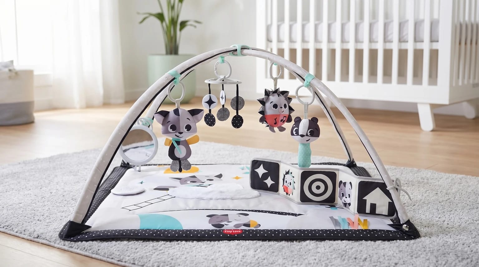 Ginásio de atividades para bebé Tiny Love, em preto e branco, montado sobre um tapete claro num quarto de bebé luminoso.