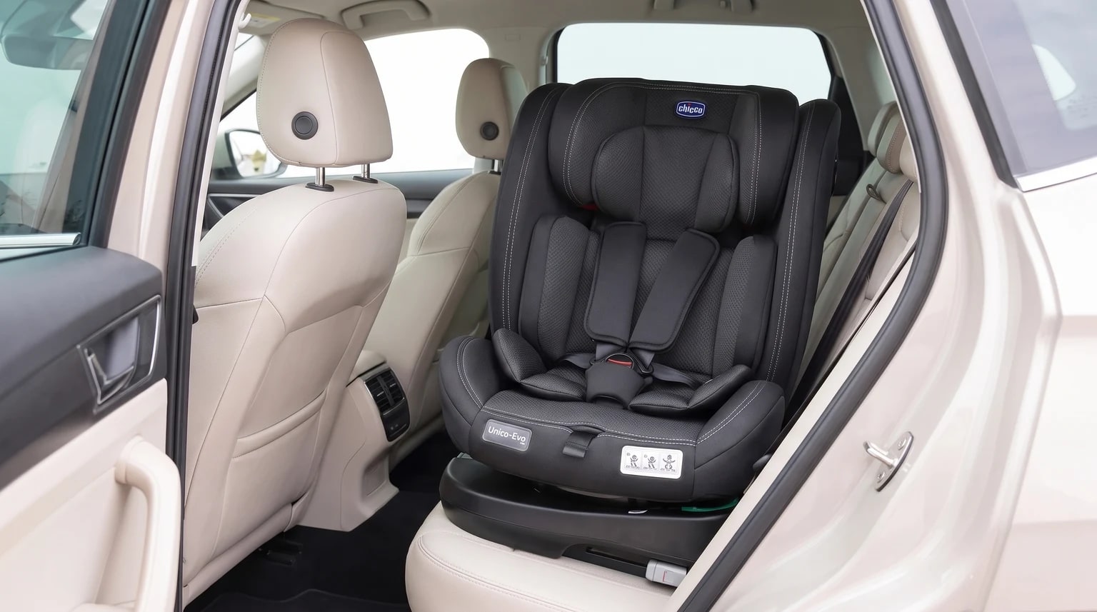 Cadeirinha Chicco Unico Evo i-Size preta posicionada no banco traseiro de um carro com interior bege.