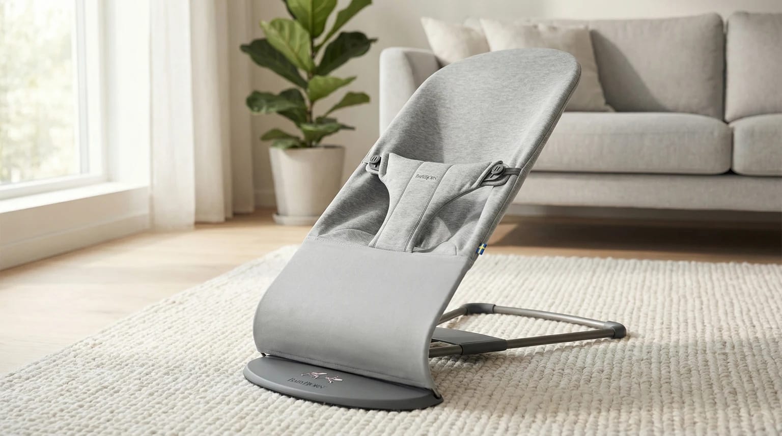 Espreguiçadeira cinzenta da BabyBjorn numa sala de estar luminosa e minimalista, sobre um tapete claro e chão de madeira.