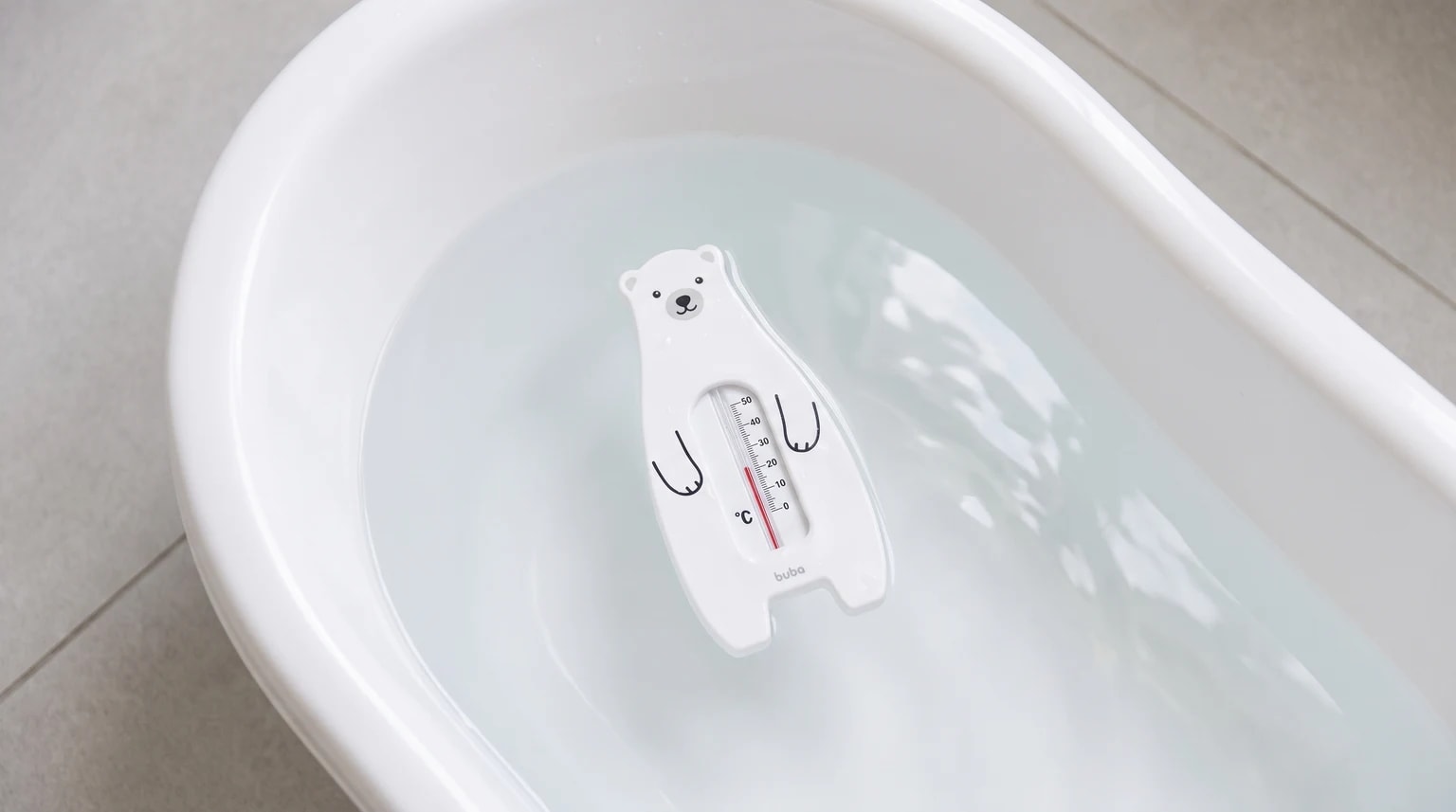 Termômetro branco em formato de urso sobre a água de uma banheira de bebê.