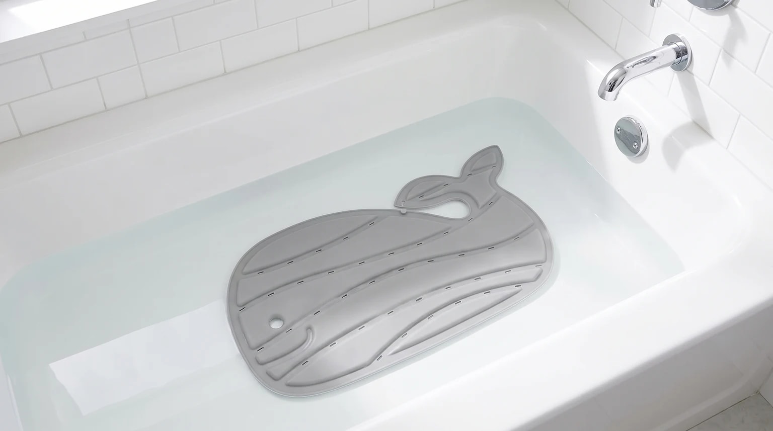 A grey, whale-shaped non-slip mat sitting at the bottom of a white bath filled with water.