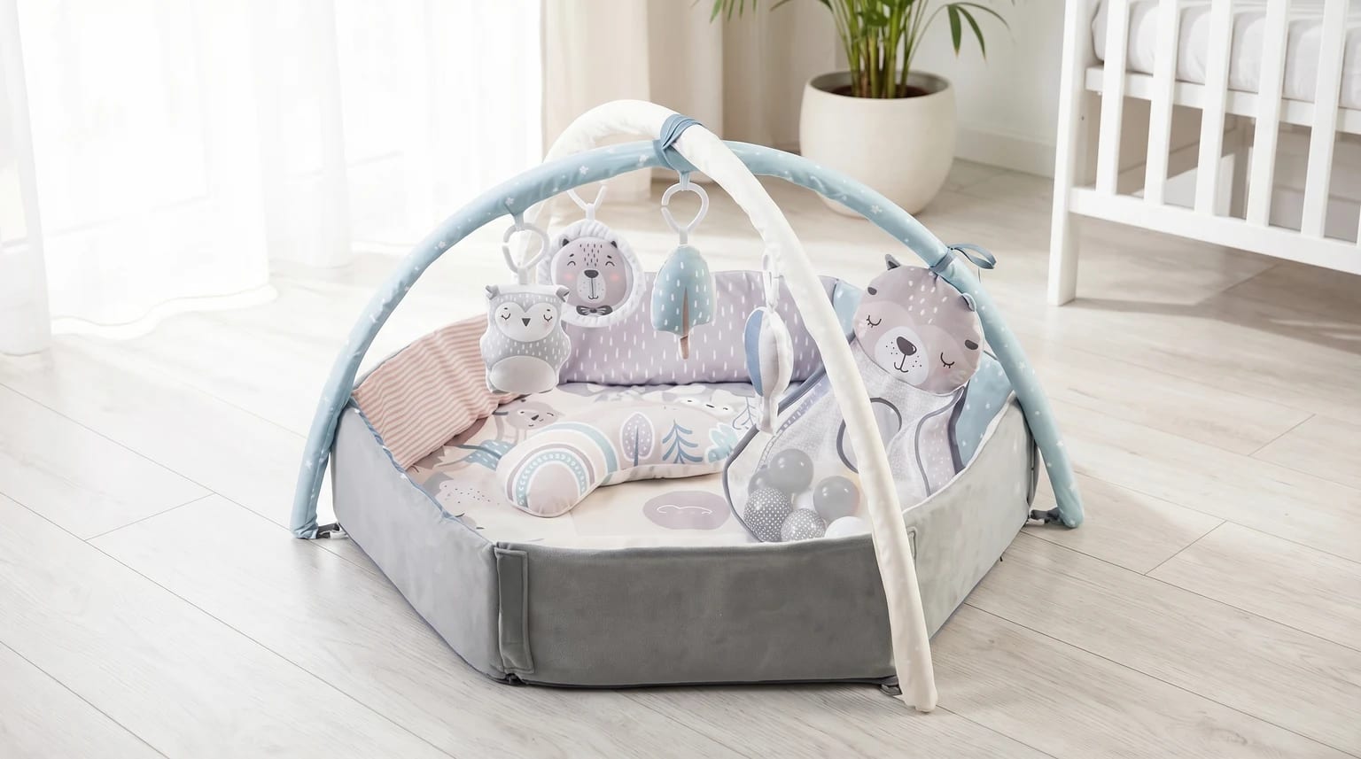 Ginásio de atividades para bebé em tons pastel, com laterais elevadas e bolas, montado no chão de madeira clara de um quarto de bebé luminoso.