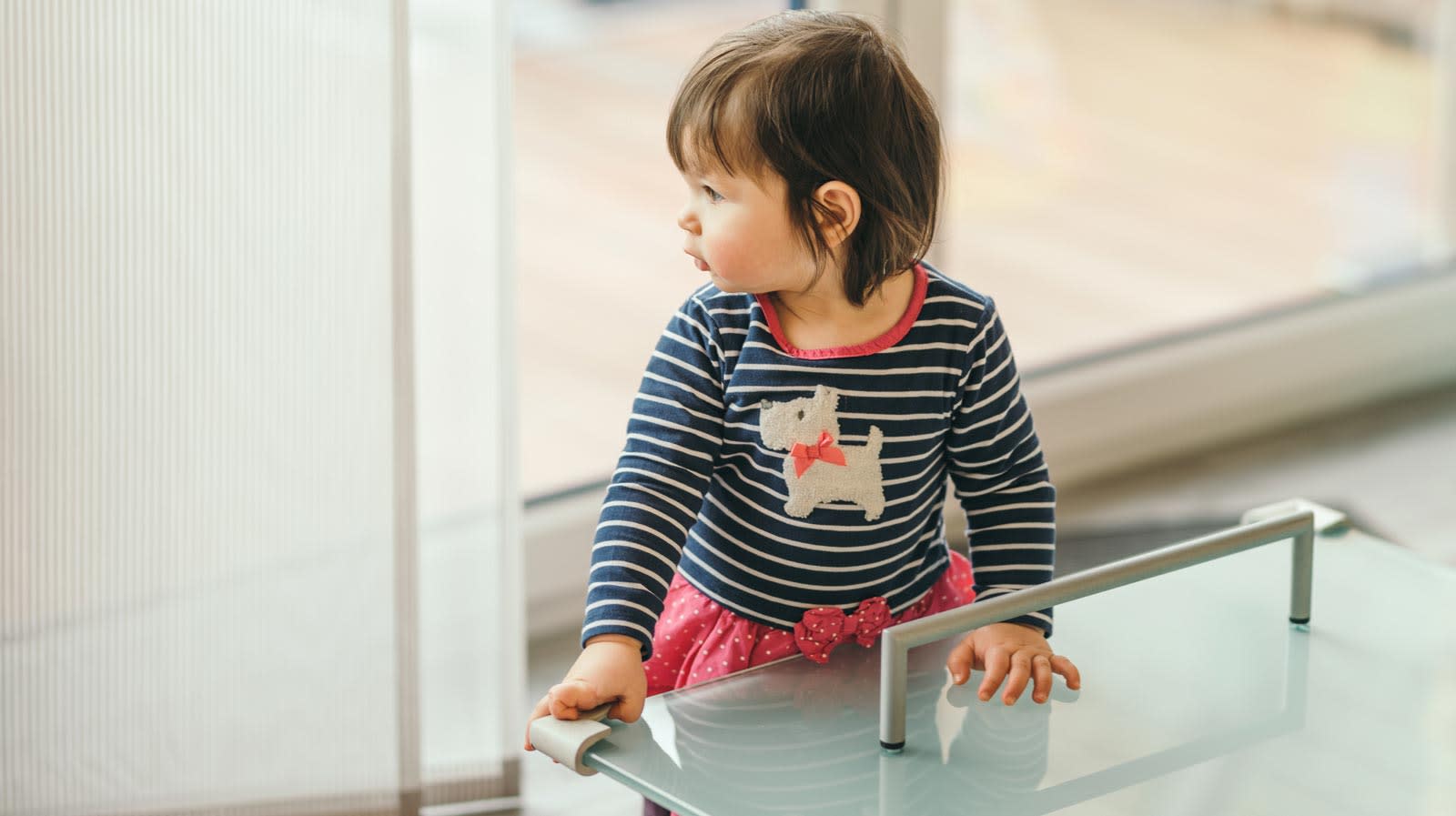 Criança em pé ao lado de uma mesa de vidro com protetor de esquina.