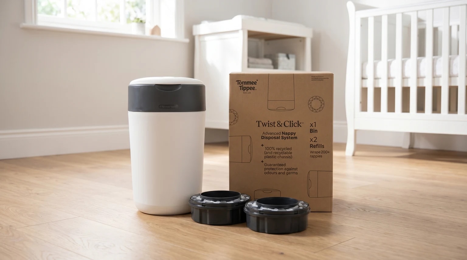 A Tommee Tippee nappy bin with its box and two refill cartridges, shown on the wooden floor of a bright nursery with a cot in the background.