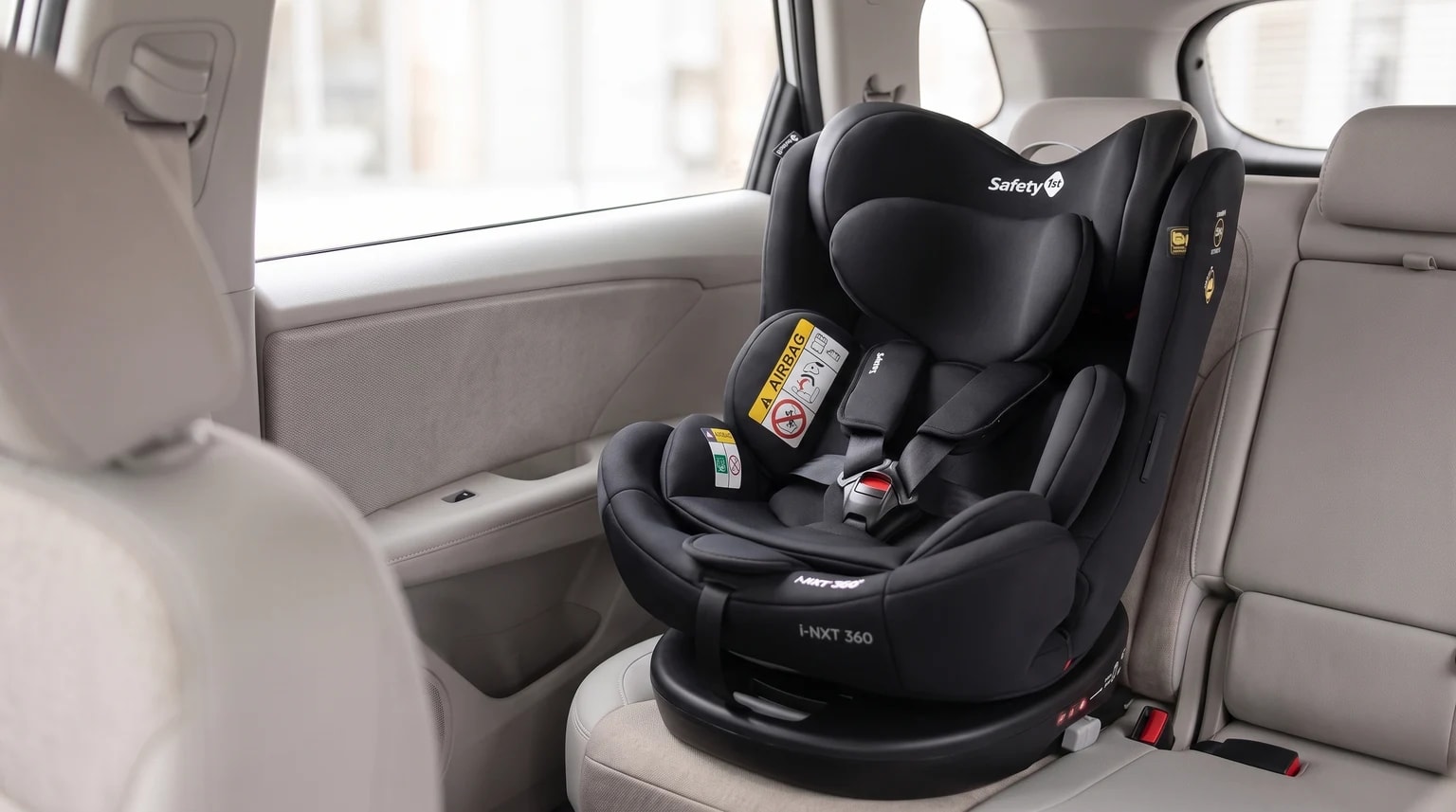 Cadeirinha Safety 1st i-NXT 360 preta posicionada no banco traseiro de um carro com interior claro.