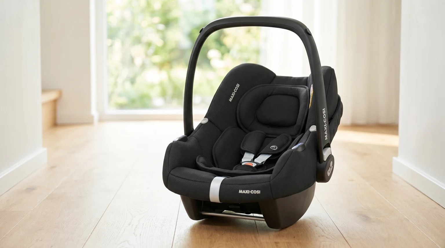 Cadeira auto Maxi-Cosi CabrioFix i-Size preta, pousada num chão de madeira clara numa casa moderna e bem iluminada.
