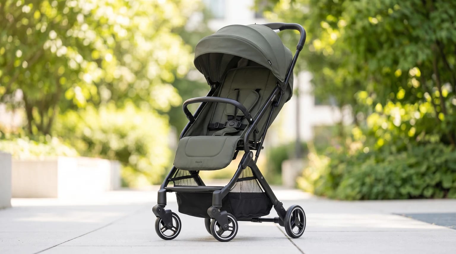 Carrinho de bebé Hauck Travel N Care em verde azeitona, num parque citadino soalheiro e moderno.