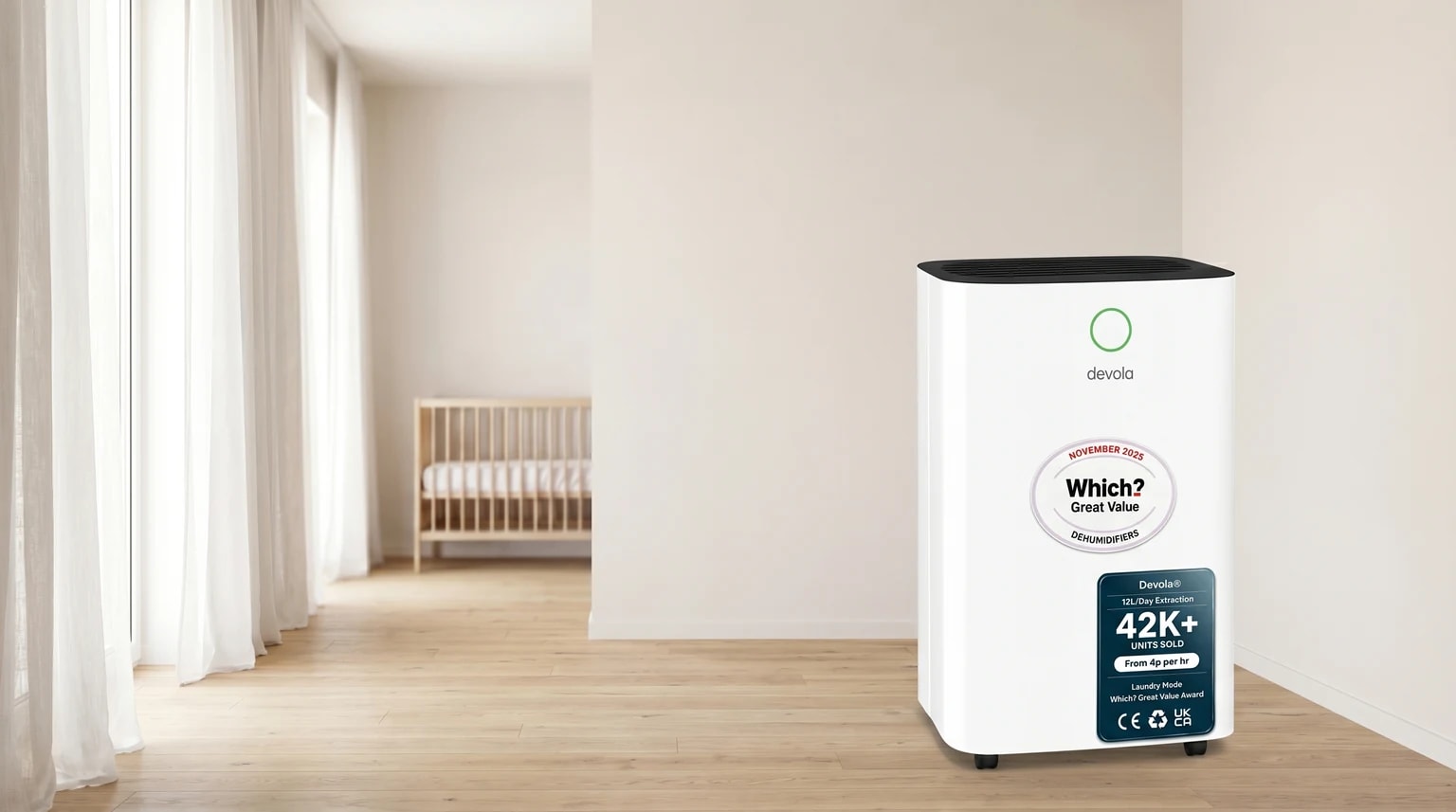 A white Devola dehumidifier on a wooden floor in a bright nursery corner, with a cot softly blurred in the background.