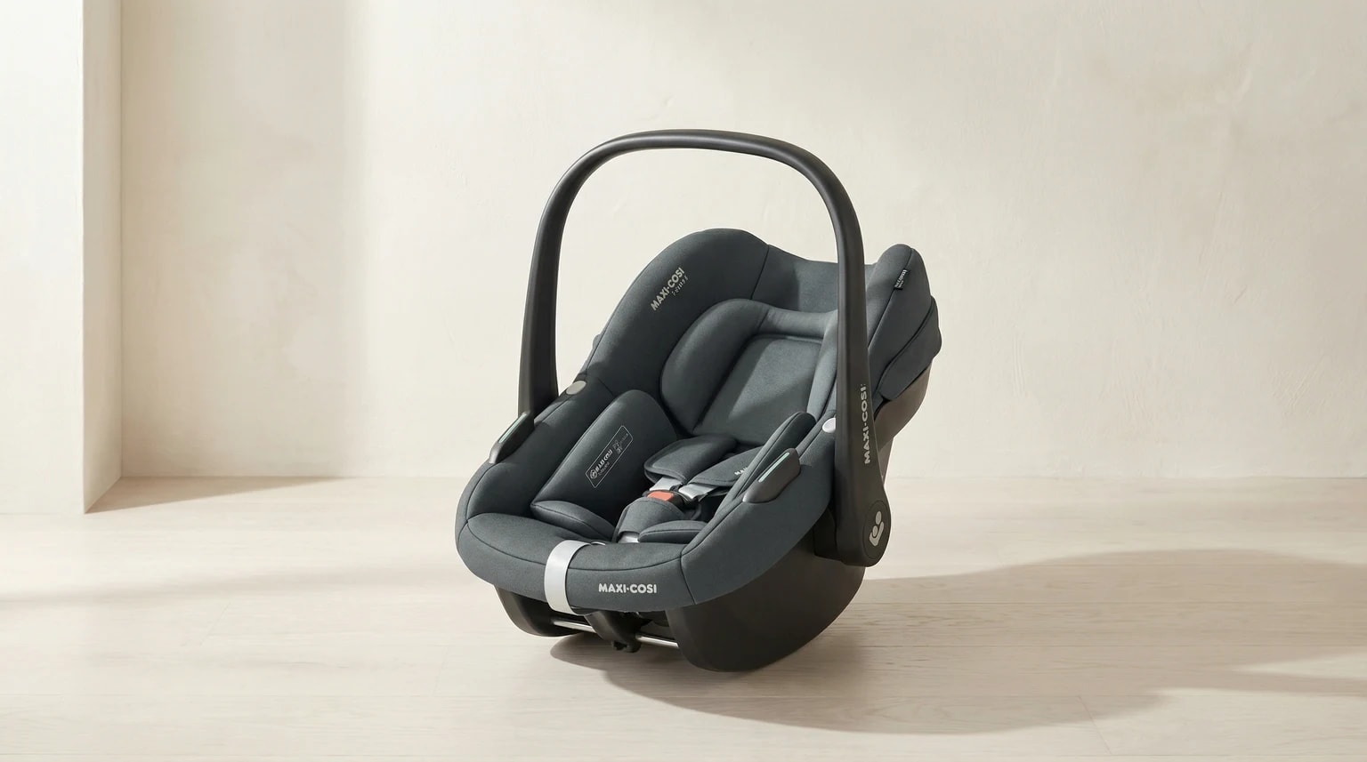 Ovo Maxi-Cosi Pebble S i-Size em cinzento escuro num ambiente interior claro com fundo editorial suave e luz natural.