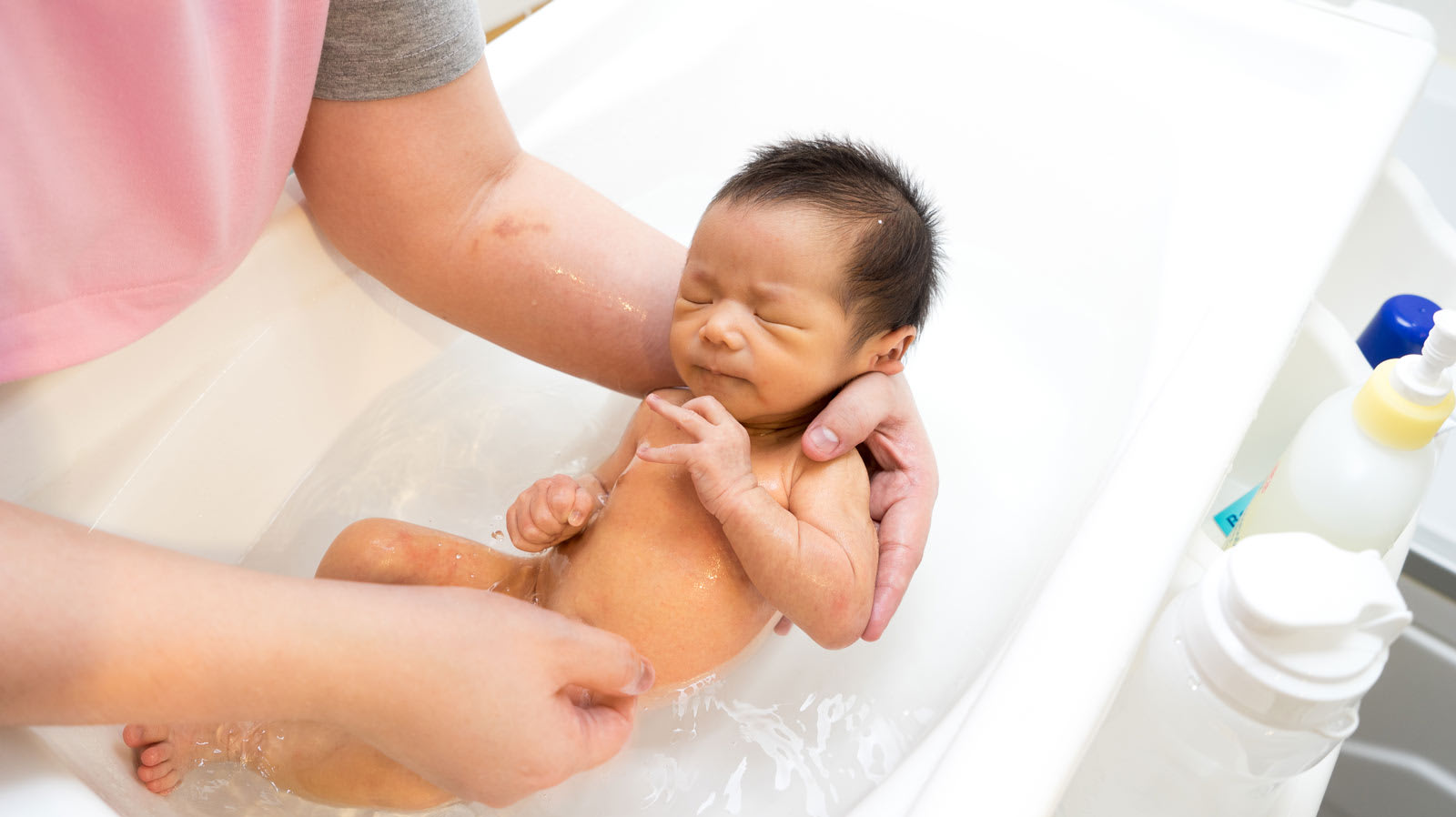 Mãe segura bebé a tomar banho em uma banheira para bebés.