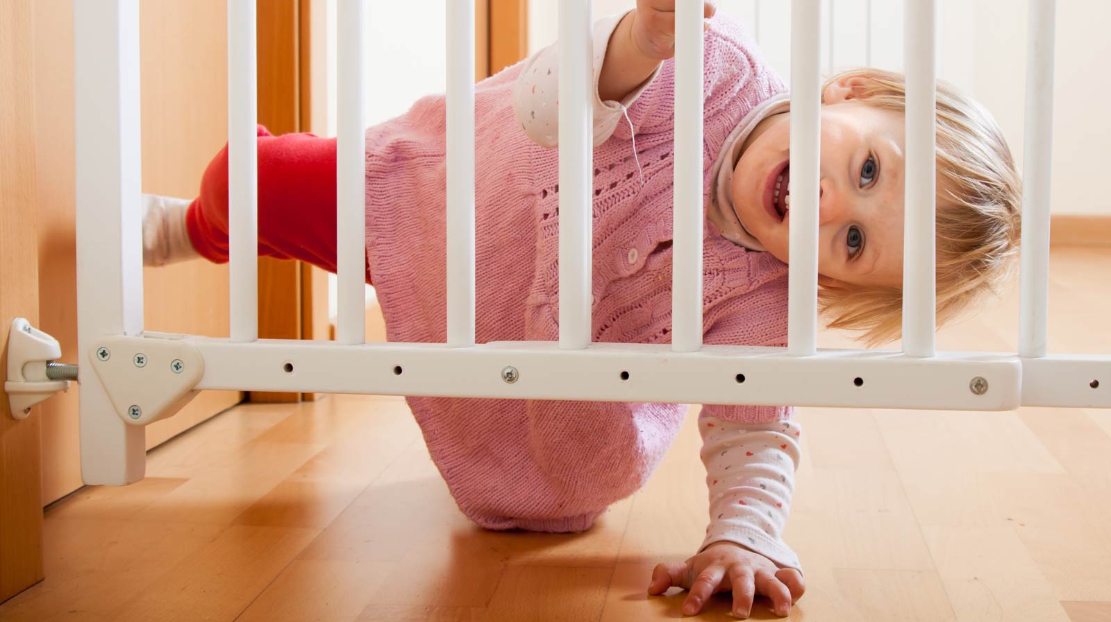 Uma bebé sorridente atrás de uma barreira de proteção para bebés.