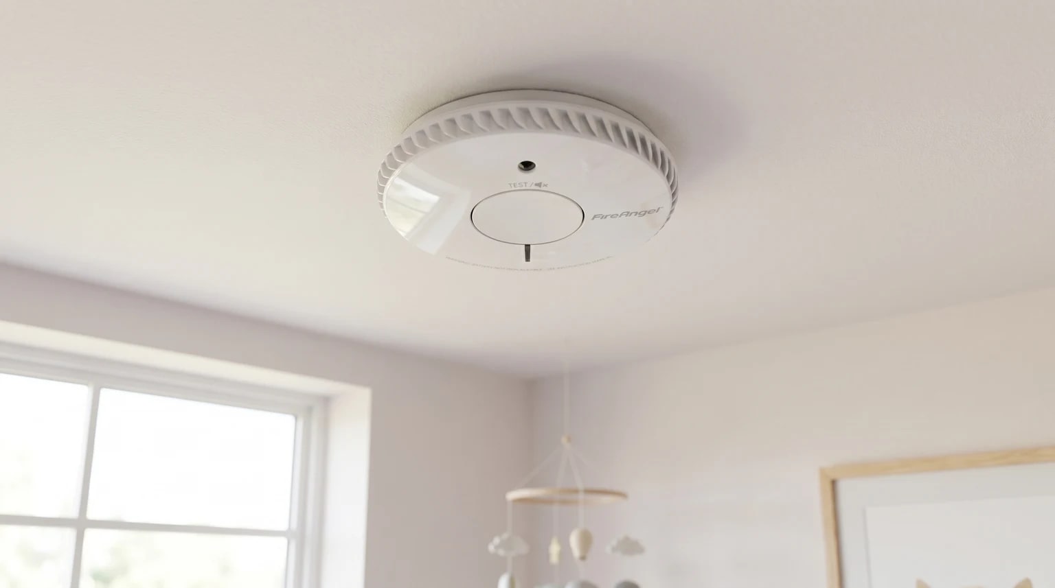 Detector de fumo FireAngel branco instalado no teto de um quarto de bebé luminoso e sereno.