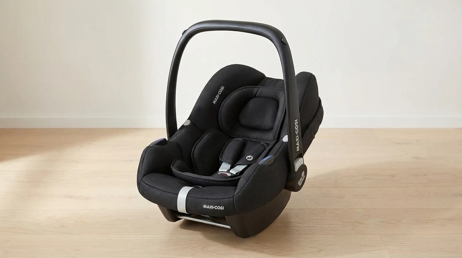 Ovo Maxi-Cosi CabrioFix i-Size preto num ambiente interior claro com parede bege suave, chão de madeira clara e luz natural.
