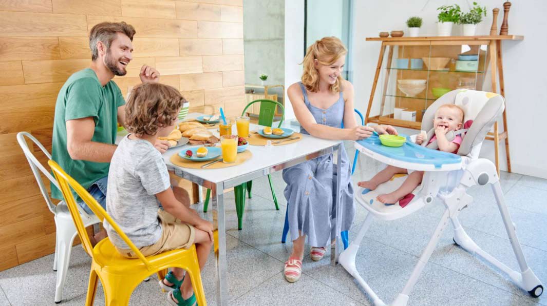 Pais comendo e mãe alimentando bebé na cadeira de refeição Kinderkfraft