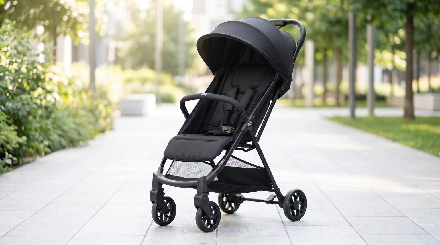 Carrinho de bebé Chicco Urbino preto, num passeio soalheiro de uma cidade moderna, com vegetação desfocada ao fundo.