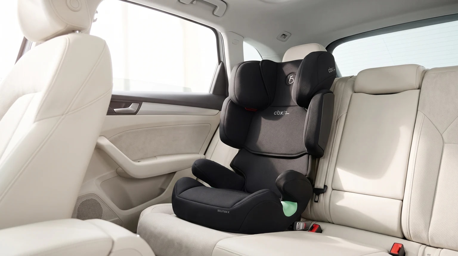 A black CBX high-back booster seat fitted on the cream leather back seat of a car.